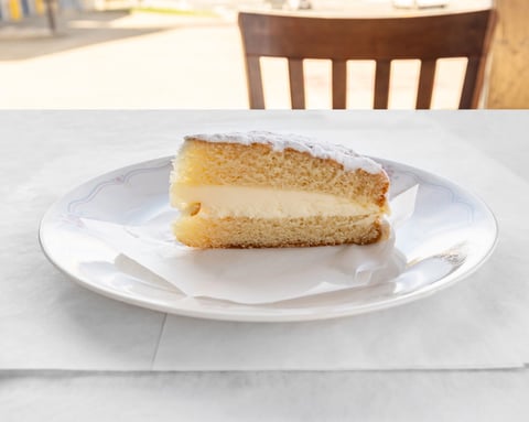 Slice of layered sponge cake with cream filling and powdered sugar on white plate with fork
