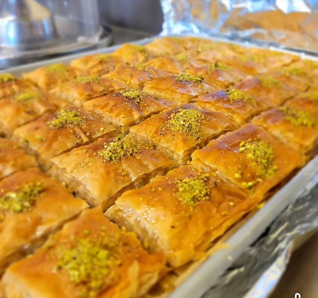 Tray of golden-brown baklava pastries topped with chopped pistachios, cut into rectangular pieces