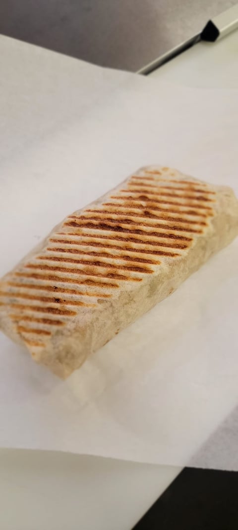 Grilled sandwich with diagonal char marks on white plate, viewed from above under indoor lighting