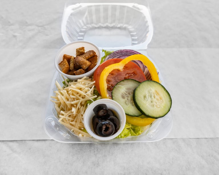 Plastic compartment tray with fried chicken, french fries, sliced vegetables, and black olives in small white bowls