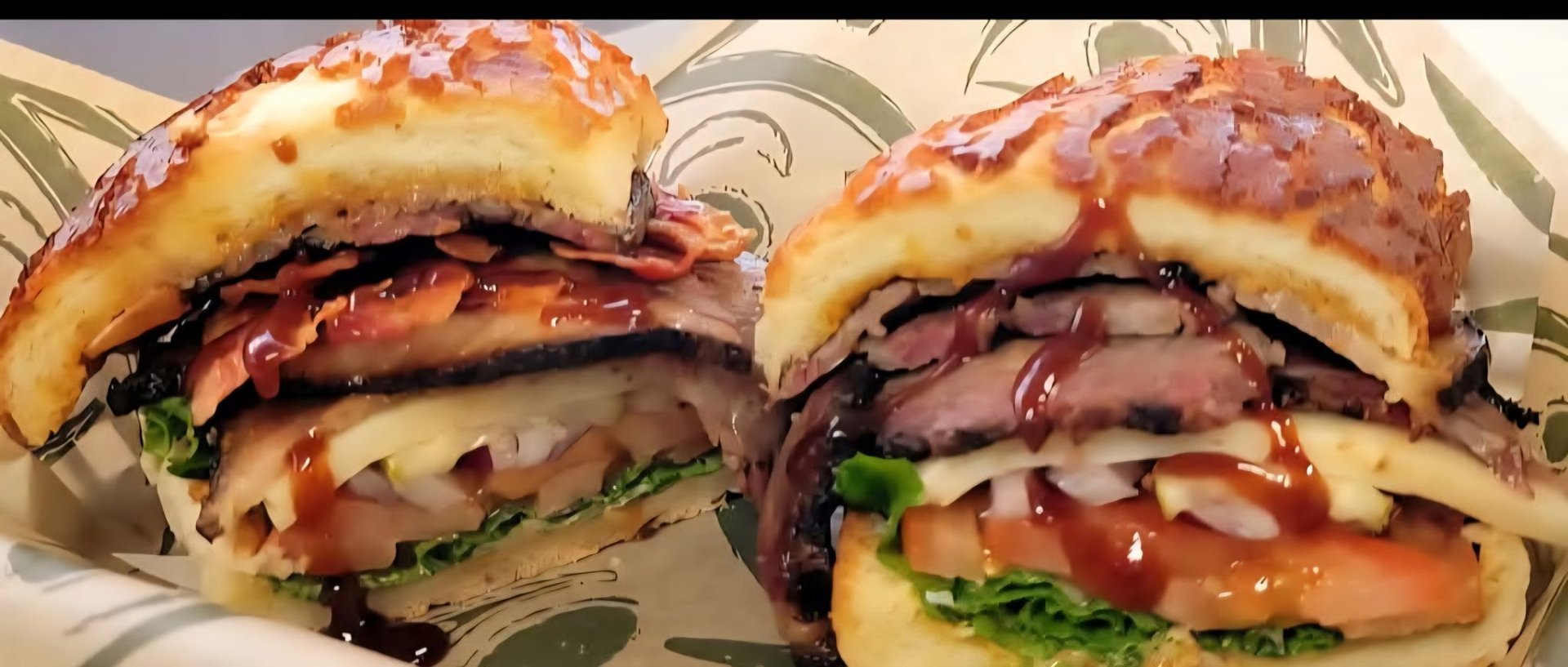 Two gourmet burgers with sesame seed buns, bacon, cheese, and fresh greens on a white plate